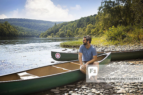 Mann schaut weg  während er auf einem Kanu am Seeufer sitzt