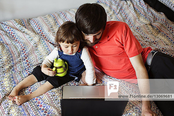 Hochwinkelansicht von Vater und Tochter  die auf einen Laptop-Computer schauen  während sie sich im Bett entspannen