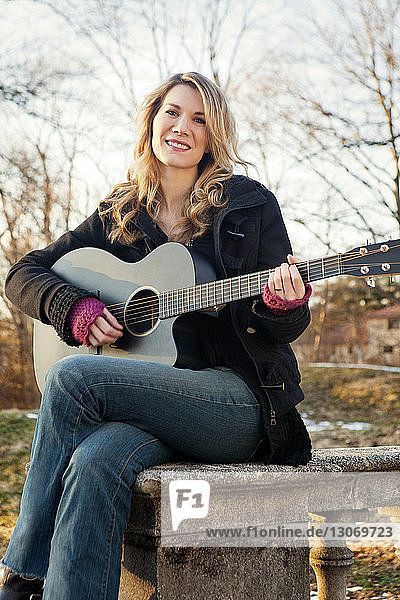 Porträt einer Frau  die Gitarre spielt  während sie auf einer Stützmauer sitzt