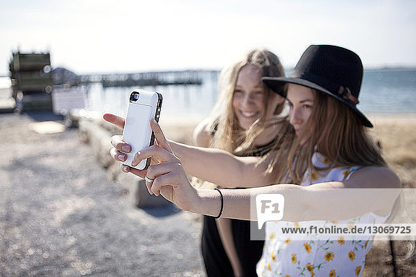 Friends taking selfie while standing against beach