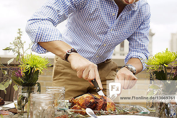 Midsection of man carving roasted chicken at table on building terrace