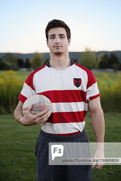 Porträt eines Spielers  der den Rugbyball auf dem Feld vor klarem Himmel hält