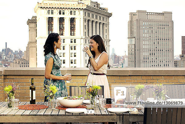 Happy friends having wine standing by food table at building terrace in city