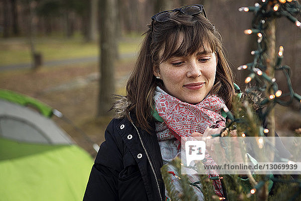 Frau schmückt Weihnachtsbaum auf Campingplatz im Wald