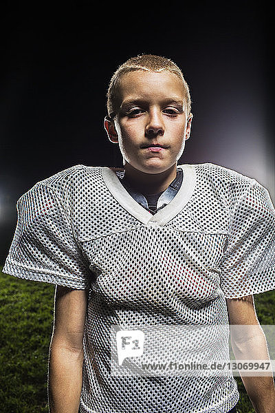 Portrait of boy in American football uniform against sky at night