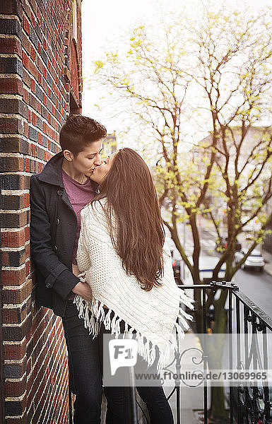 Zärtliches lesbisches Paar küsst sich im Stehen auf dem Balkon