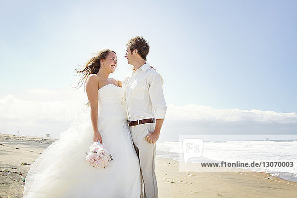 Newlywed couple standing at beach against sky