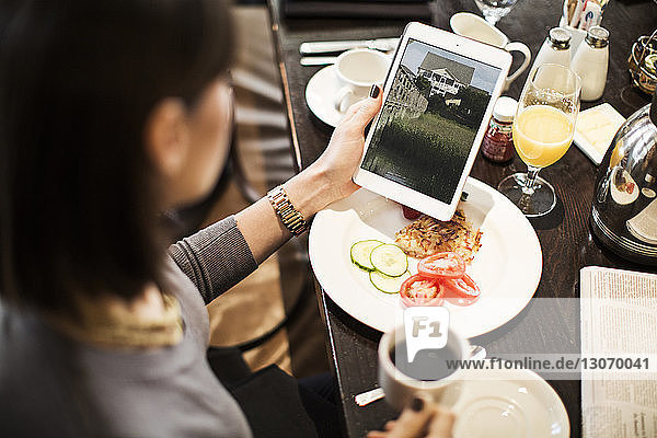 Hochwinkelansicht einer Frau  die einen Tablet-Computer benutzt  während sie im Restaurant am Tisch sitzt