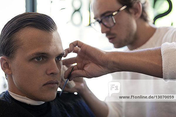 Friseur schneidet jungen Mann die Haare im Friseursalon