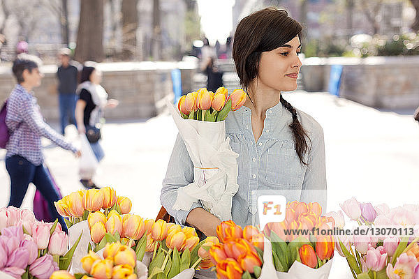 Frau mit Tulpenblüten schaut weg  während sie auf dem Blumenmarkt steht