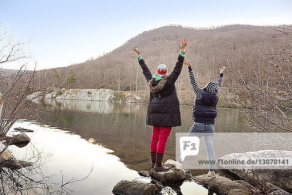 Rückansicht von Freunden mit erhobenen Armen auf einem Felsen am See stehend