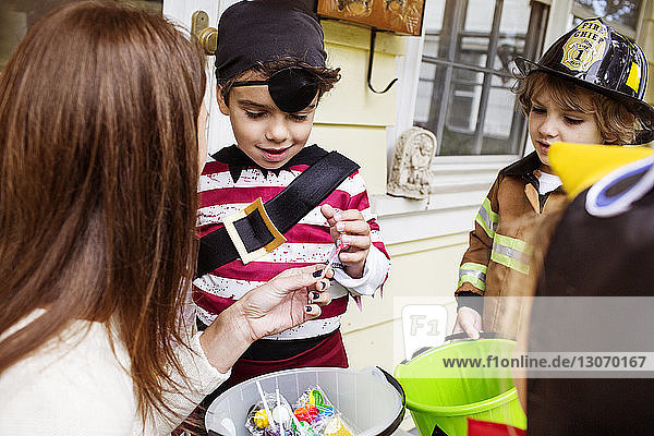 Frau verschenkt Süßigkeiten an Kinder in Halloween-Kostümen während Trick oder Behandlung