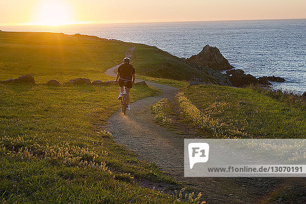 Rear view of man cycling on road against sea during sunrise