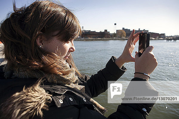 Side view of woman photographing through mobile phone while traveling in ferry