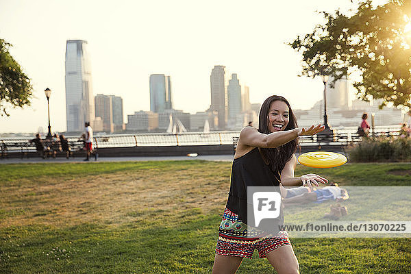 Glückliche Frau fängt Plastikscheibe  während sie im Park vor klarem Himmel steht