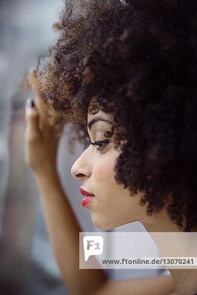 Close-up of thoughtful woman with curly hair looking through window