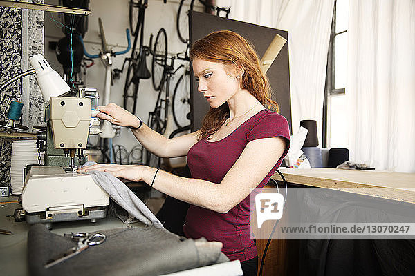 Serious fashion designer working on sewing machine at workshop