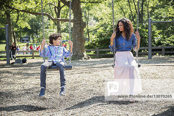Mother and son looking at each other while playing swing in park