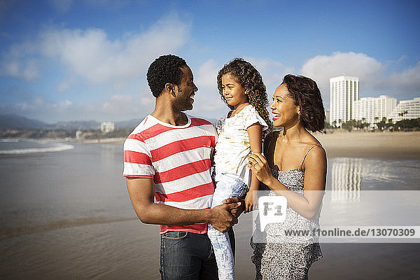 Happy parents looking at daughter while standing on shore at beach