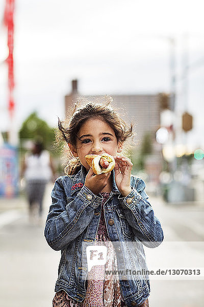Mädchen isst Hot Dog im Stehen auf der Straße in der Stadt
