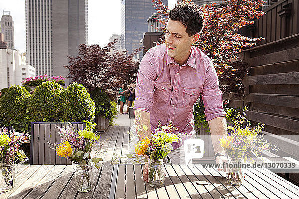 Mann arrangiert Blumenkrüge auf Holztisch im Hof der Stadt
