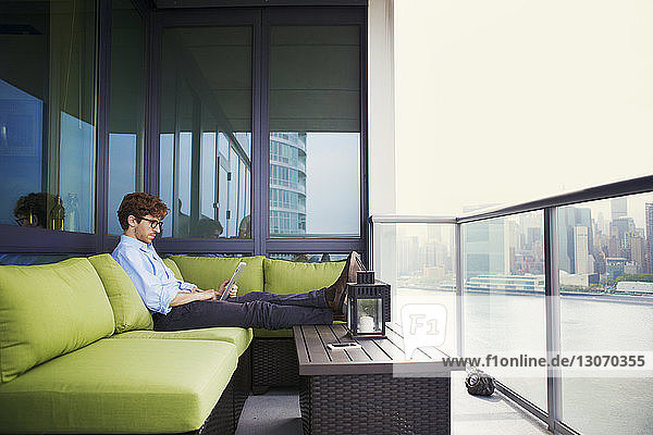 Side view of businessman using tablet computer while sitting on sofa at office balcony