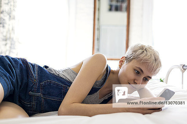 Frau benutzt Smartphone  während sie sich zu Hause im Bett entspannt