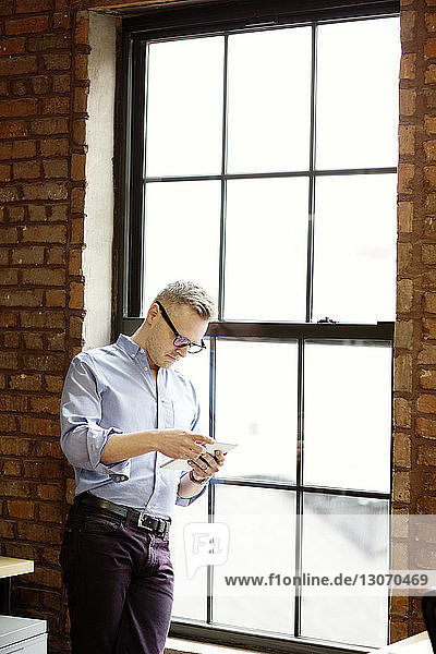 Businessman using tablet computer while standing by window in office