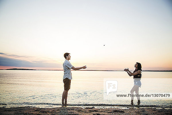 Freunde spielen mit Stein am Strand gegen den Himmel bei Sonnenuntergang