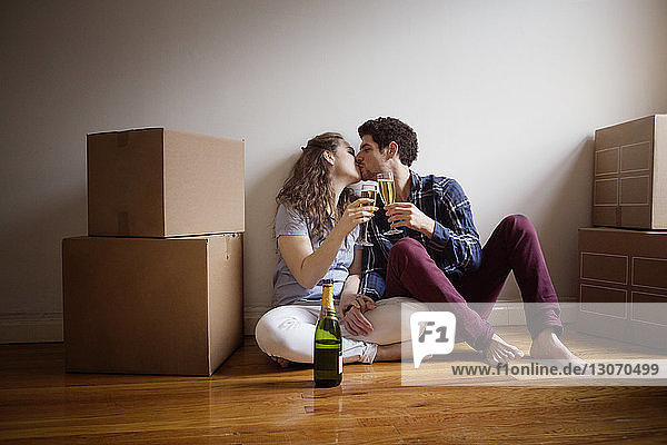 Paar mit Weingläsern  die sich küssen  während sie zu Hause auf dem Boden sitzen