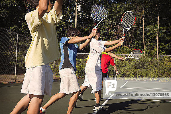 Players standing in row playing tennis against fence at court