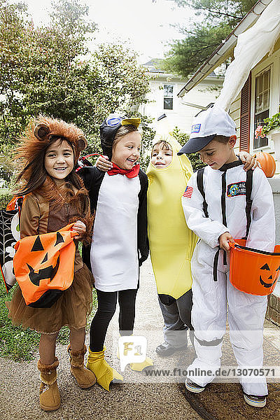 Fröhliche Kinder in Halloween-Kostümen in voller Länge  die während eines Streichs oder einer Behandlung im Hof stehen