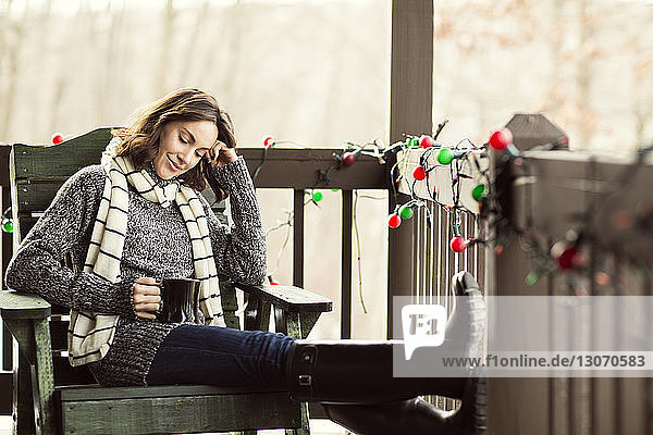 Frau hält Kaffeetasse lächelnd in der Hand  während sie auf einem Holzstuhl sitzt