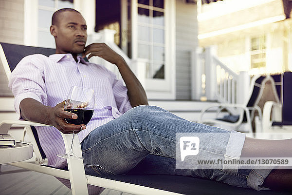 Nachdenklicher Mann hält Weinglas  während er auf einem Liegestuhl sitzt