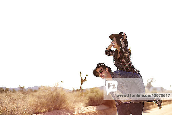 Glücklicher Mann nimmt Huckepack mit seiner Freundin gegen den klaren Himmel