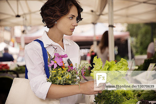 Frau mit Blumen kauft Salat auf dem Markt
