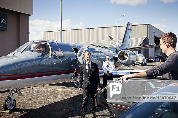 Mann schaut Geschäftsmann und Pilot an  während er auf dem Flugplatz neben dem Auto steht