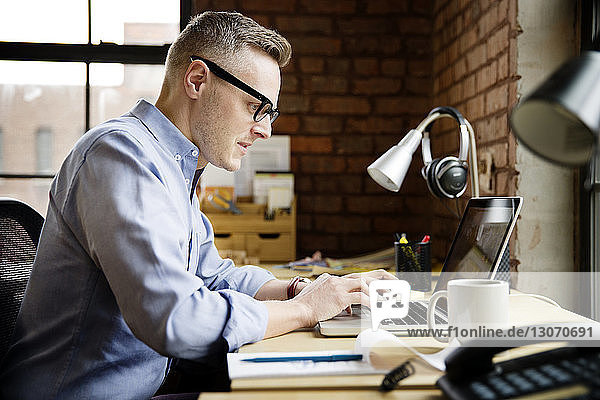Seitenansicht eines Geschäftsmannes bei der Arbeit an einem Laptop-Computer im Büro