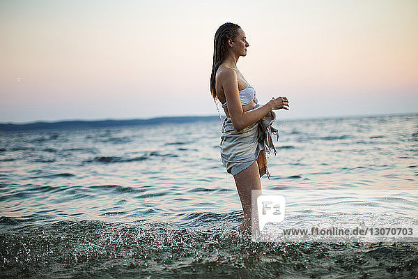 Side view of woman looking away while standing in sea