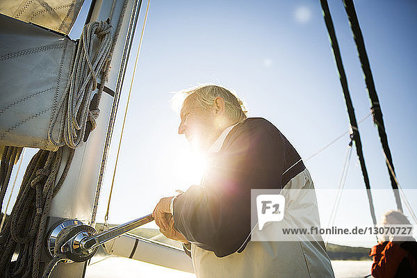 Seitenansicht eines älteren Mannes  der im Sommer den Griff einer Yacht gegen den Himmel dreht