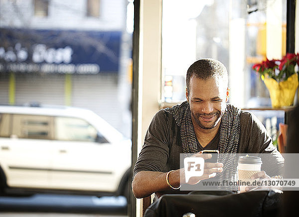 Mann benutzt Mobiltelefon  während er im Cafe sitzt