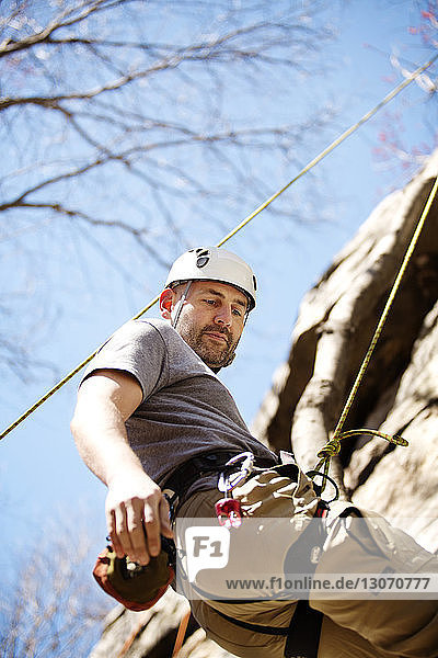 Side view of man rappelling on rock face