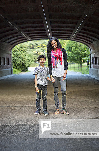 Porträt von Mutter und Sohn  die sich an den Händen halten  während sie unter einem Tunnel im Park stehen