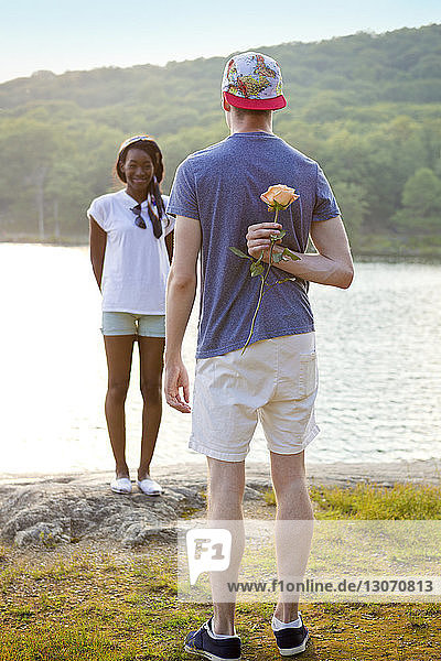Rear view of man hiding rose behind back to propose girlfriend