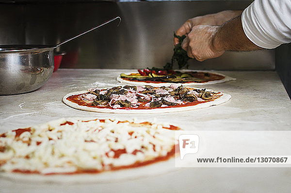 Cropped image of hands putting toppings on raw pizza
