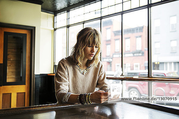 Frau benutzt ein Smartphone  während sie an einem Tisch in einer Bar sitzt