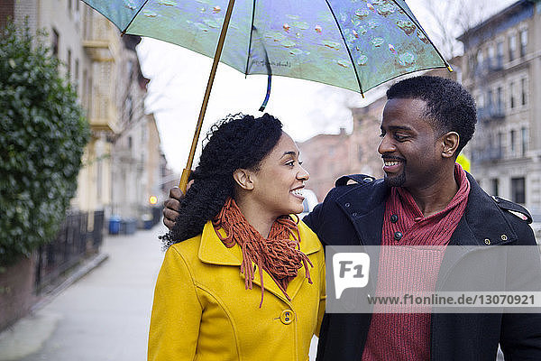 Mann hält Regenschirm  während er mit Frau auf der Straße in der Stadt unterwegs ist
