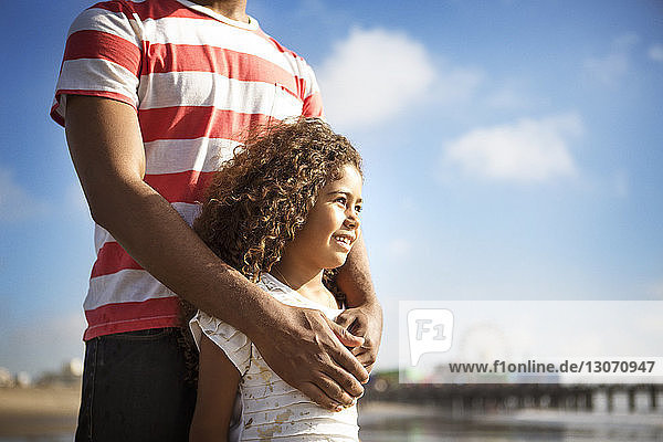 Mittendrin stehender Mann mit Tochter am Strand gegen den Himmel