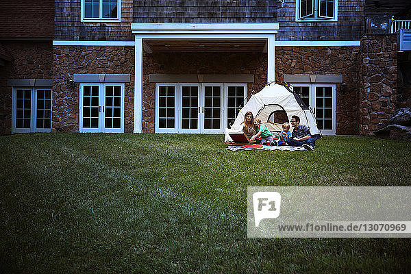 Familie isst Pizza  während sie im Zelt auf einem Grasfeld vor dem Haus sitzt