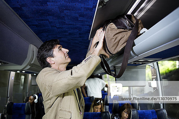 Man putting bag in luggage rack while standing in bus